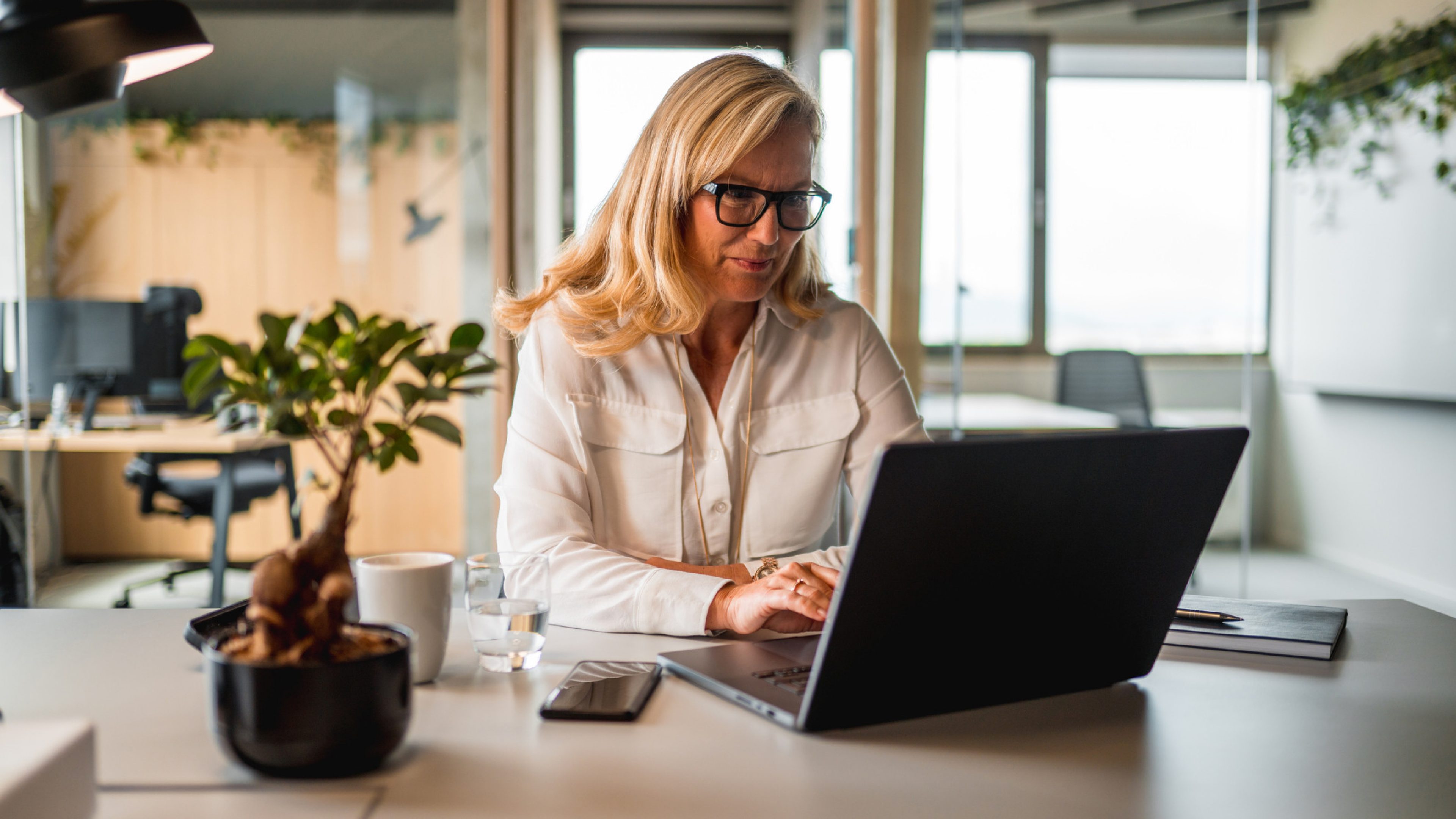 Mature caucasian female working alone in the office. She is wearing casual clothes and using a laptop.