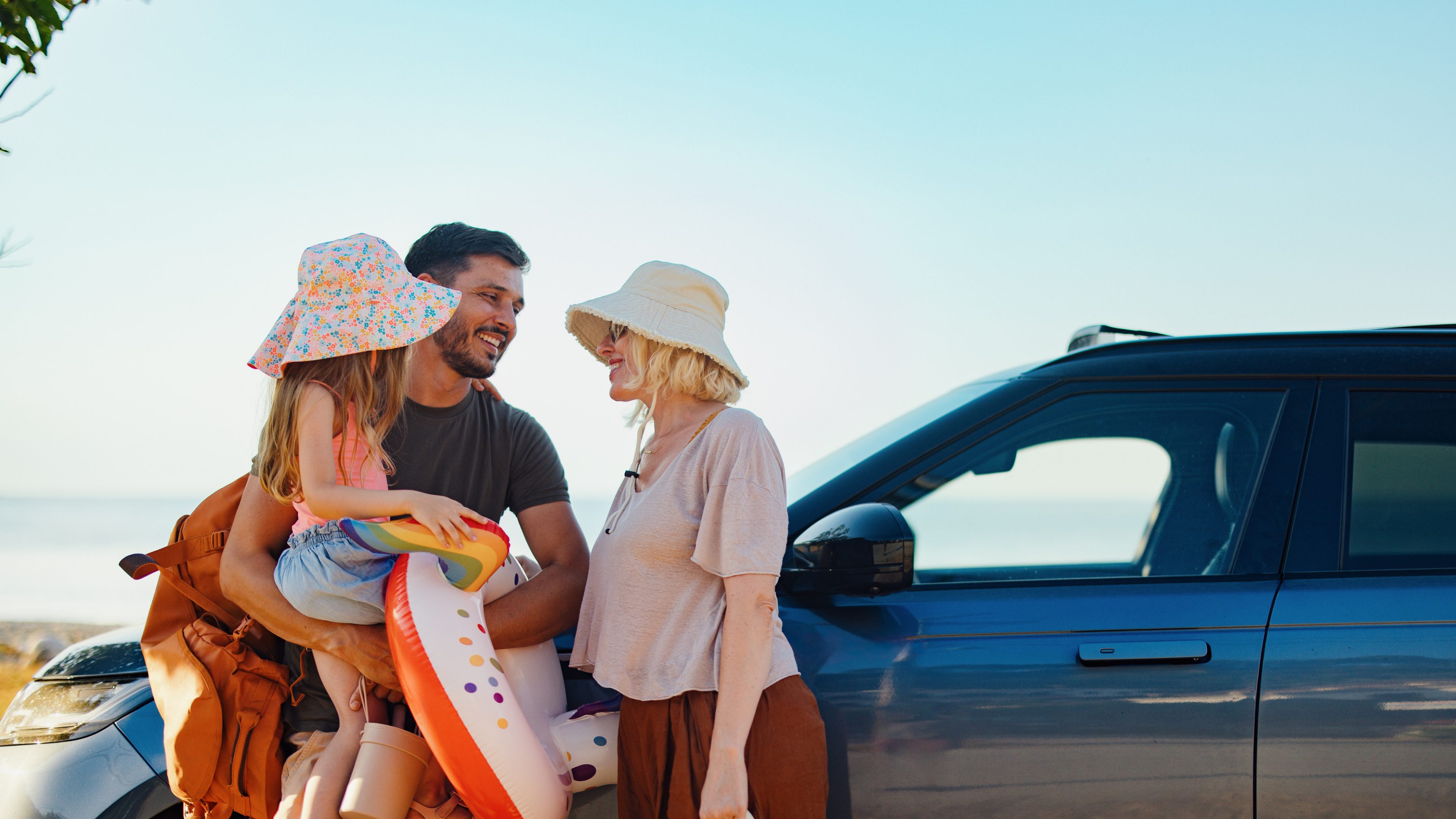 A cheerful family gathers near their car beside the sea, ready for a fun vacation. The sun shines brightly as they prepare with beach gear, symbolizing carefree summer days filled with joy.