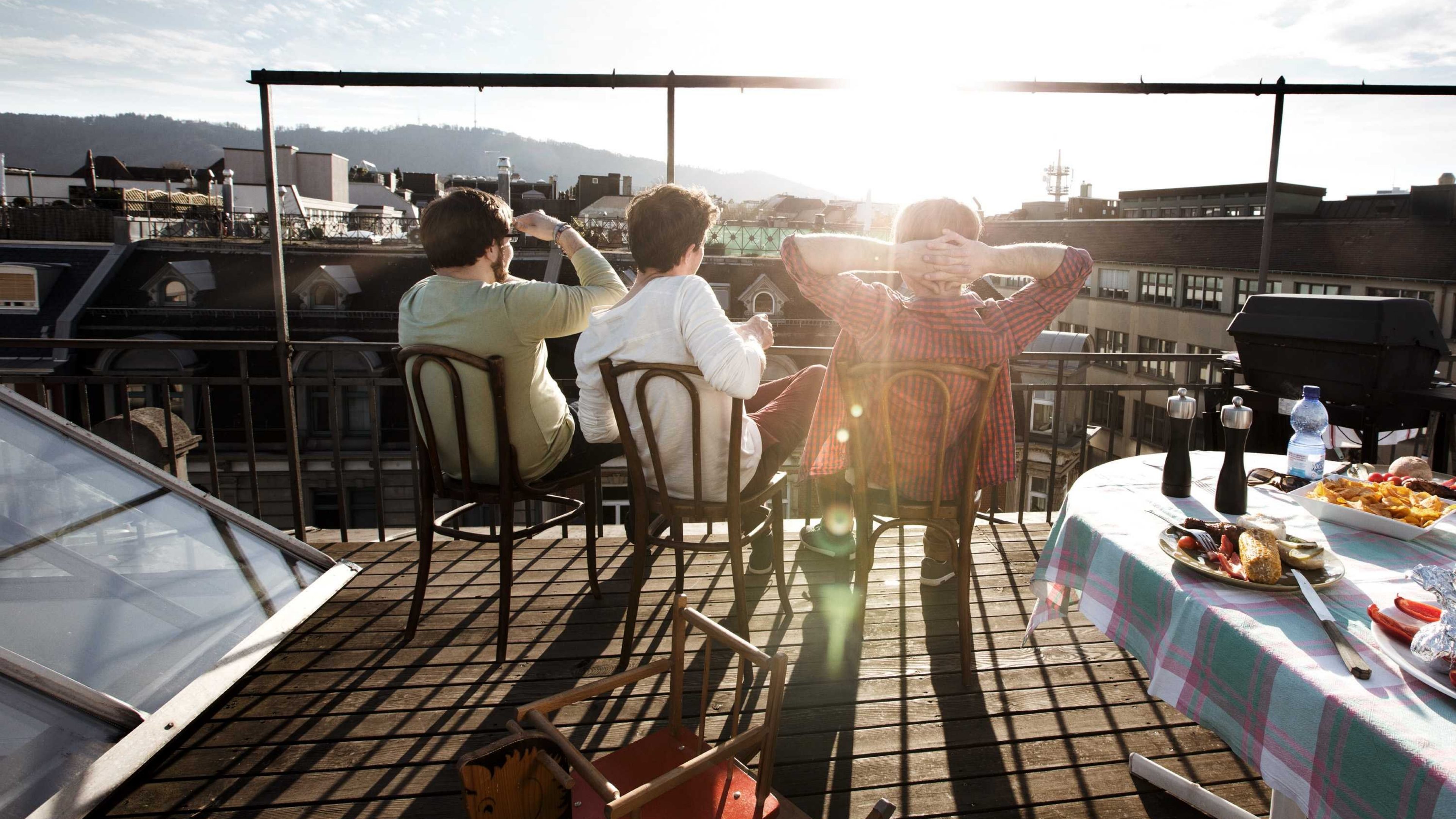 Freunde sitzen gemeinsam auf Dachterrasse und betrachten Sonnenuntergang